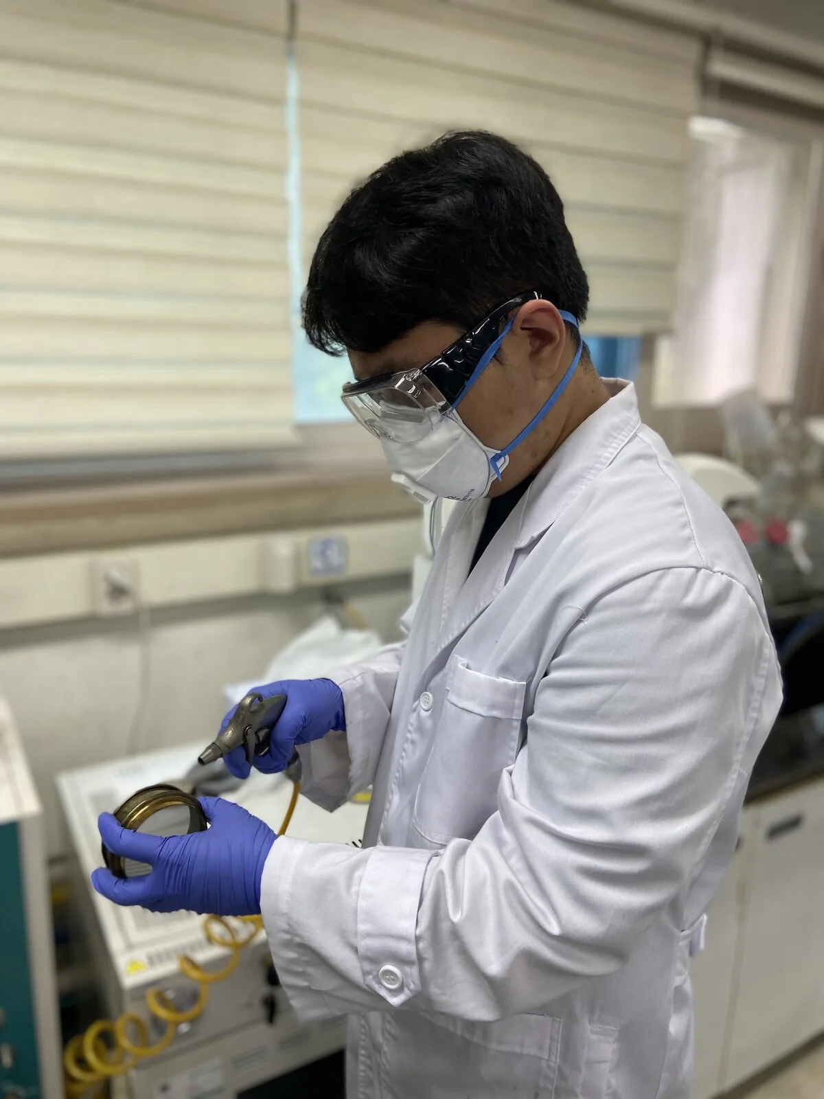 One Choi in a lab coat, goggles and gloves handling a sample at the bench.