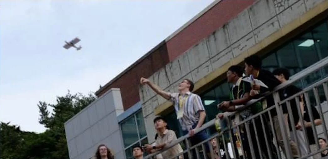 Students on the terrace launching their planes, one already up against the sky.