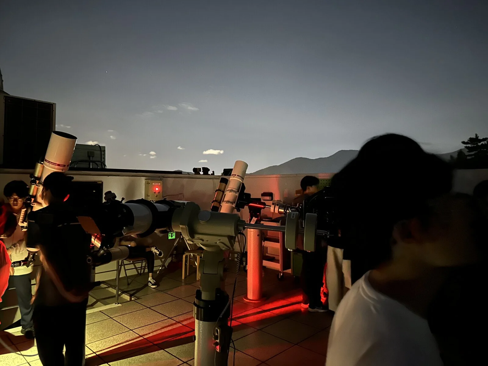 An evening observation session — telescopes on the rooftop deck at dusk, mountains behind.